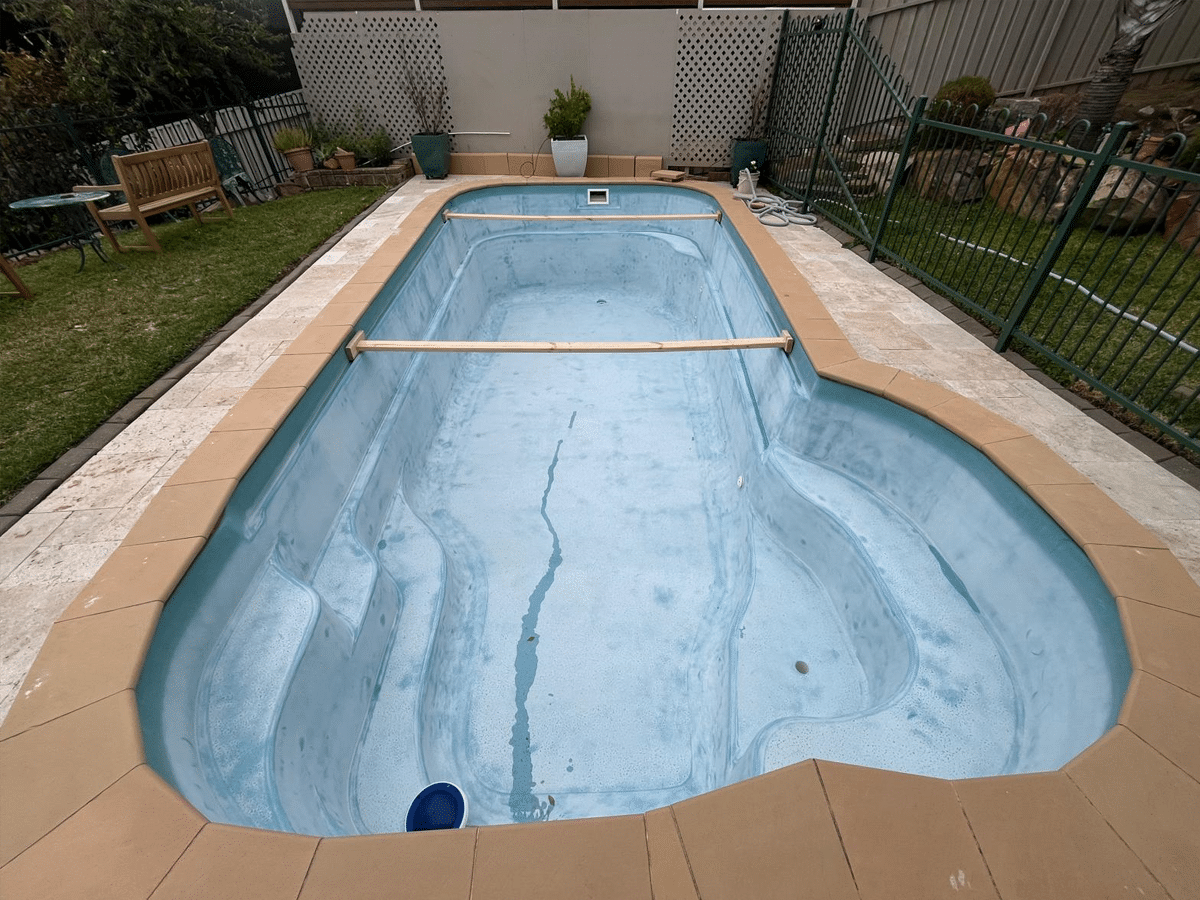 Faded and stained fibreglass pool in Adelaide backyard before resurfacing — worn blue-grey surface with visible streaks